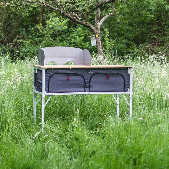 Compacte kampeerkeukenkast met houten blad en spatscherm, opgesteld in het gras